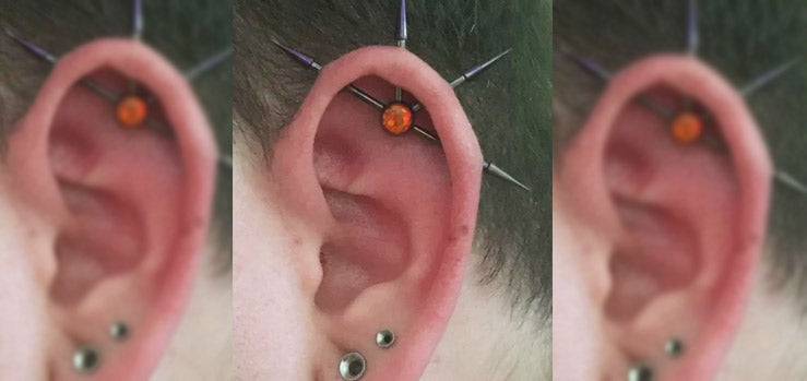 Three views of an ear with a four-point industrial piercing, spiked bars meeting at an orange opal, plus lobe studs