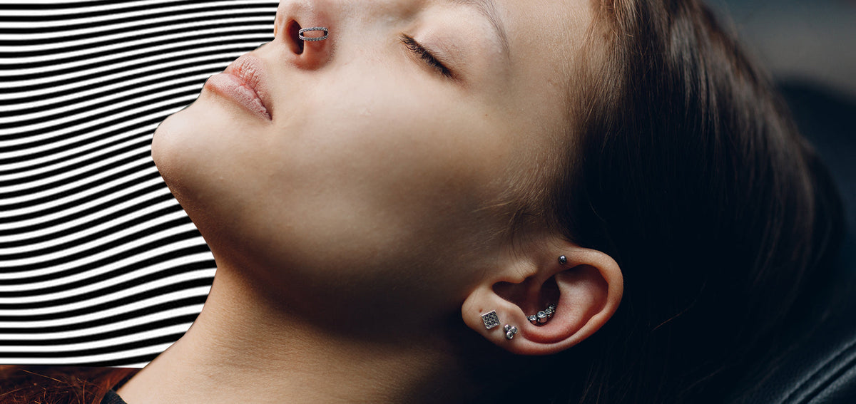 Woman with her head tilted back and eyes closed, wearing a jeweled septum clicker and crystal studs in her ear