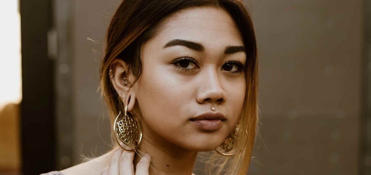 Woman wearing gold-tone filigree ear weights, several studs up her ear cartilage, a nostril stud and a philtrum stud