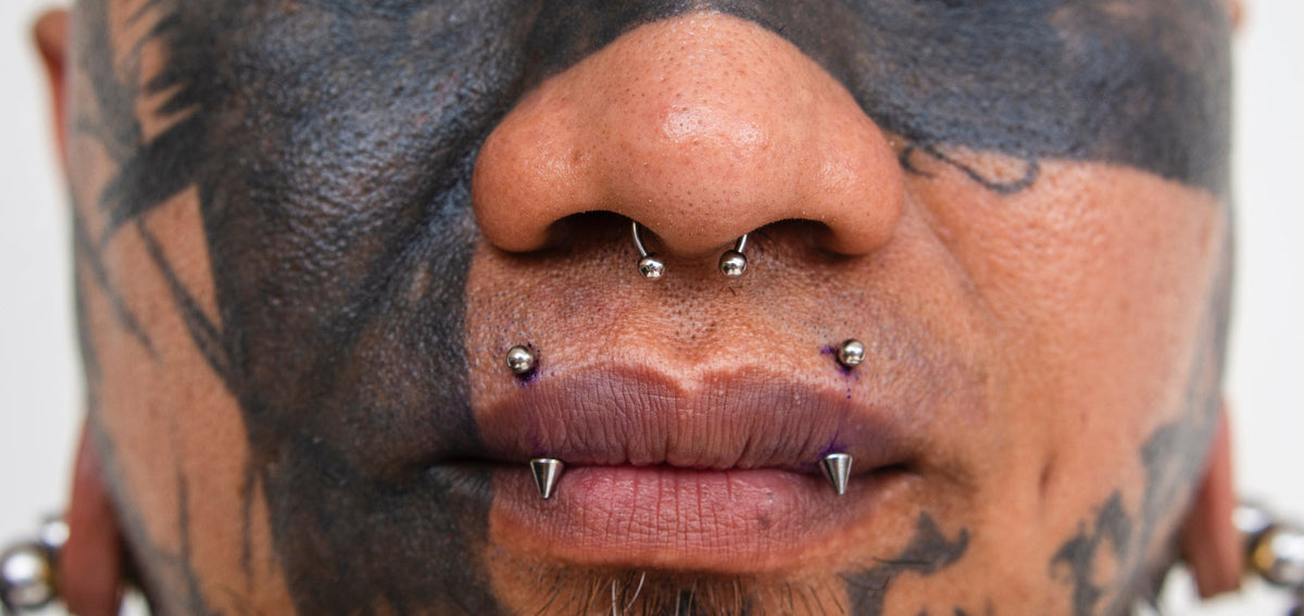 Tattooed face with a septum ring and spike-ended angel fang barbells through both sides of the upper lip