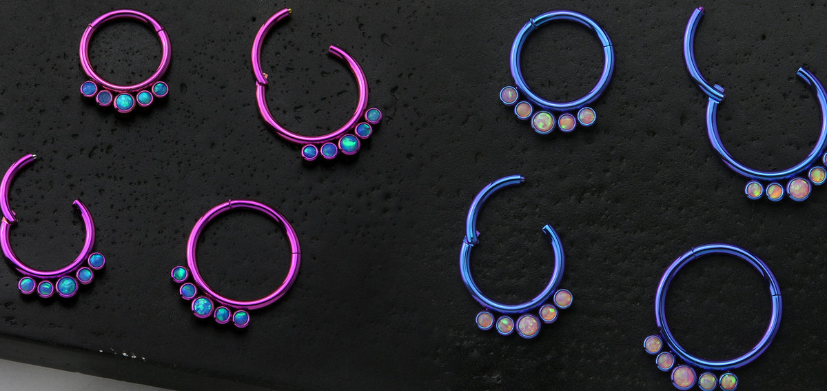 Pink and blue anodized hinged segment rings with a row of opalescent stones, on a black surface