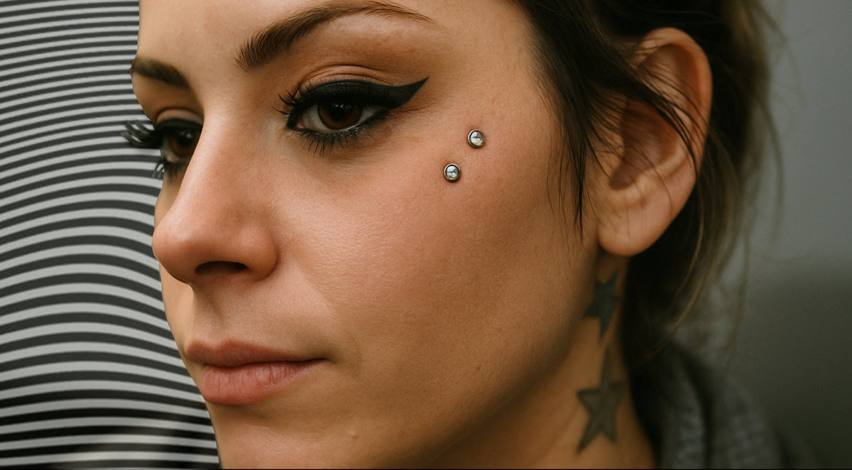 Woman with winged eyeliner and an anti-eyebrow piercing, two silver-tone beads on her upper cheek below the eye