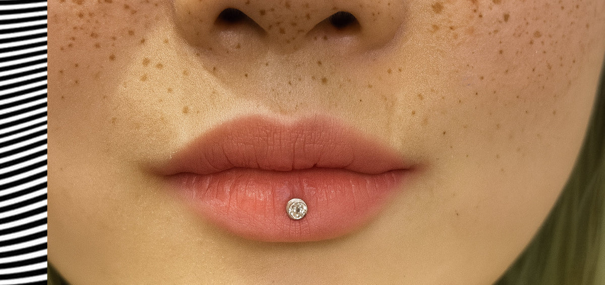 Close-up of freckled lips with a single crystal stud in the center of the lower lip
