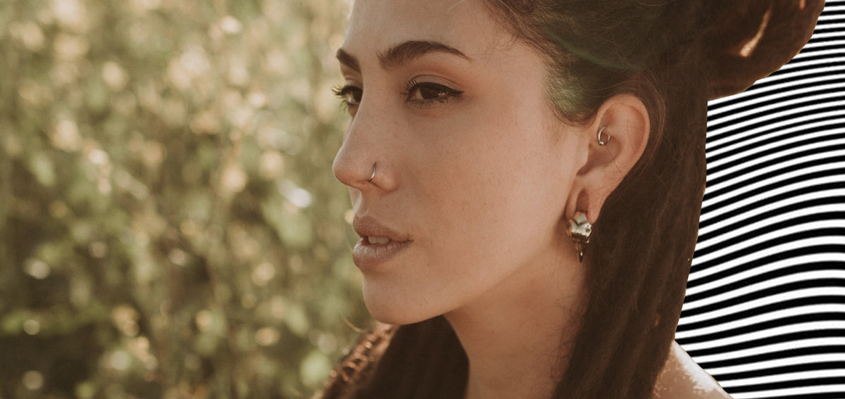 Woman with locs piled up, a thin nostril hoop, a small ring in her rook and a sculpted metal earring in her lobe