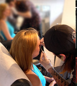 Gloved piercer in a black cap marking a spot on a blonde client's face in a piercing studio