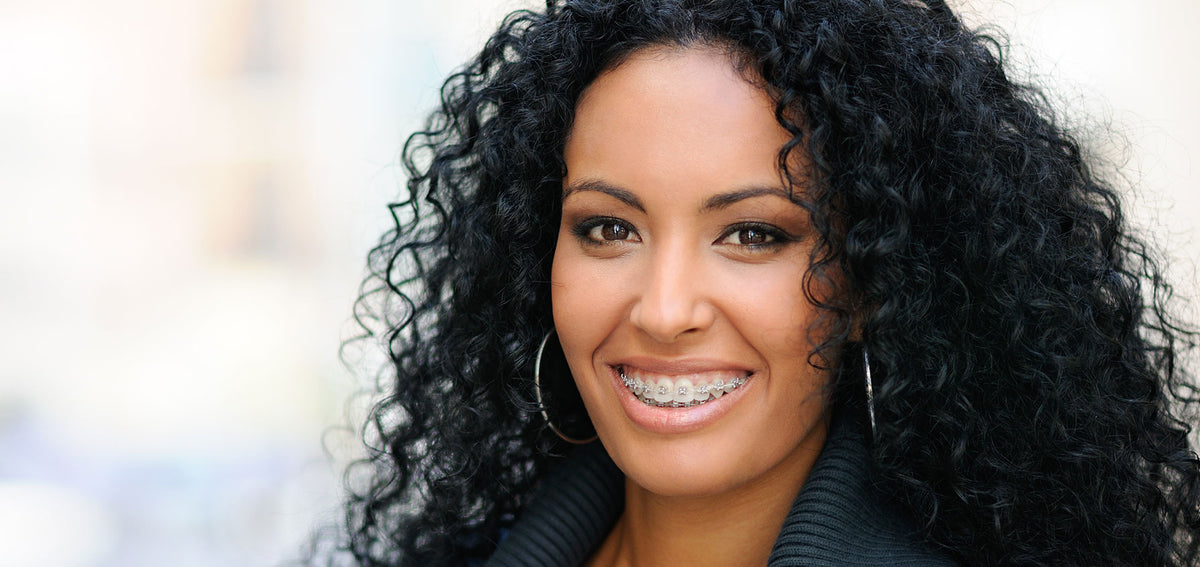 Smiling woman with long curly black hair, dental braces and large silver-tone hoop earrings