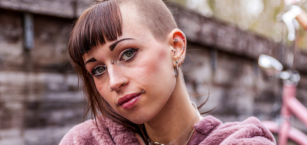 Woman with a bridge piercing, hoops in both nostrils, studs around her lips and many hoops and studs along her ear