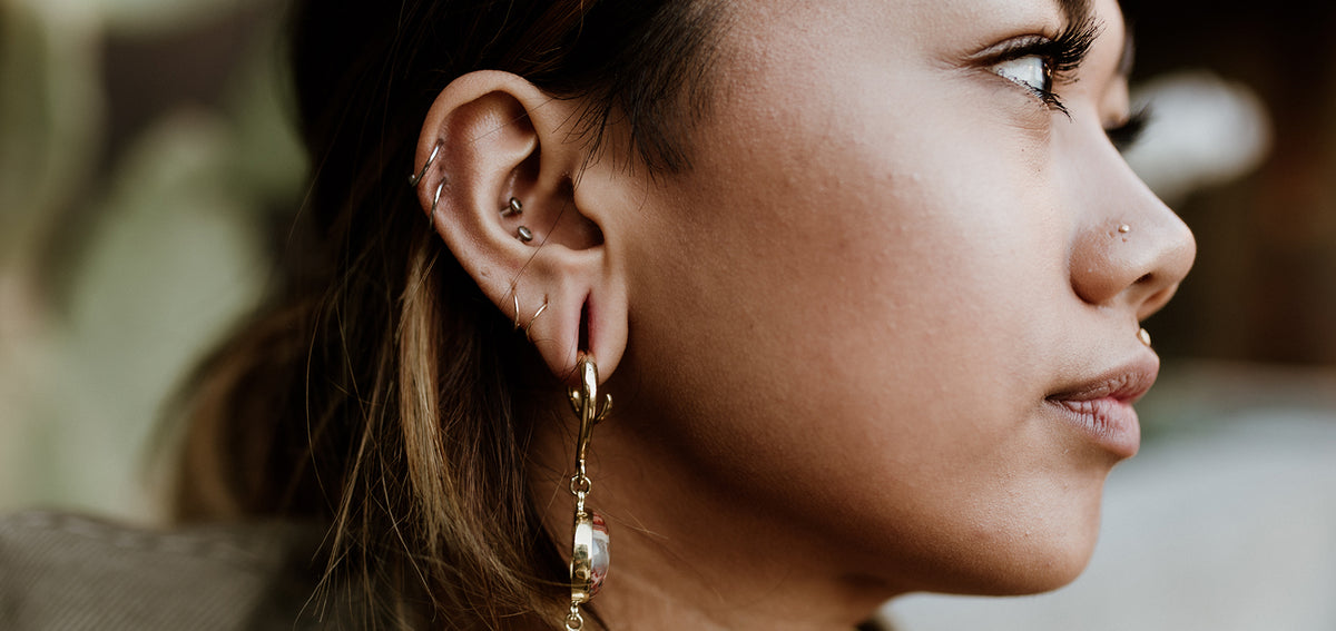 Woman in profile with helix hoops, conch studs, small lobe hoops, a nostril stud and a long gold-tone drop earring