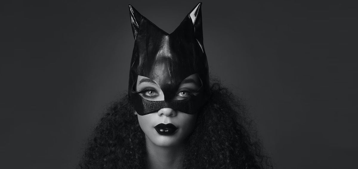 Black and white portrait of a woman in a glossy cat-eared mask with dark lipstick and voluminous curly hair