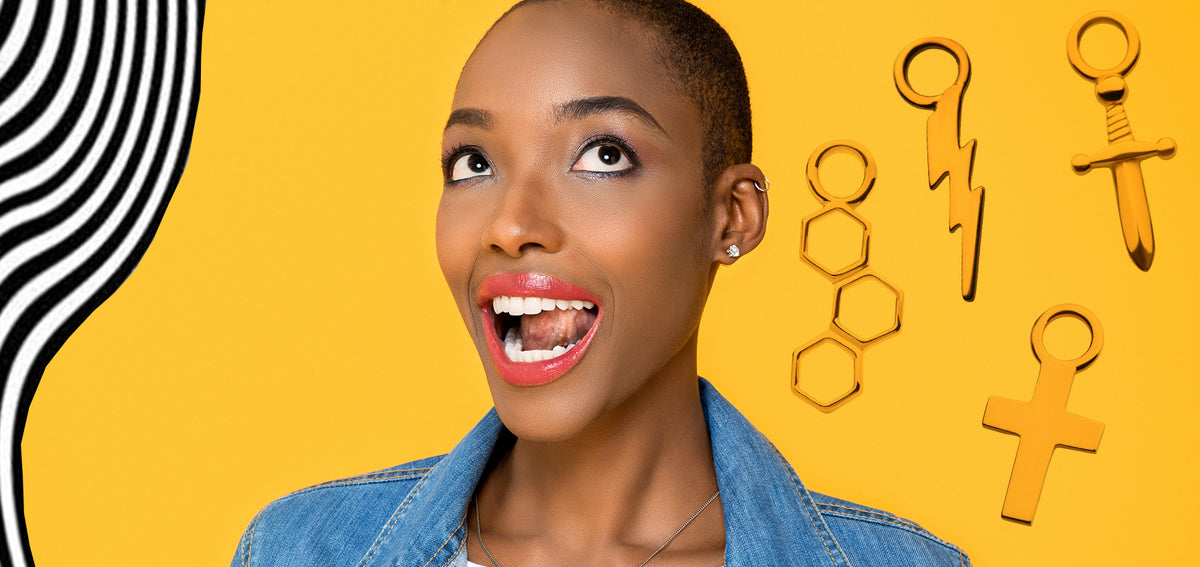 Smiling woman on a yellow background beside gold-tone hexagon, lightning bolt, sword and cross charms
