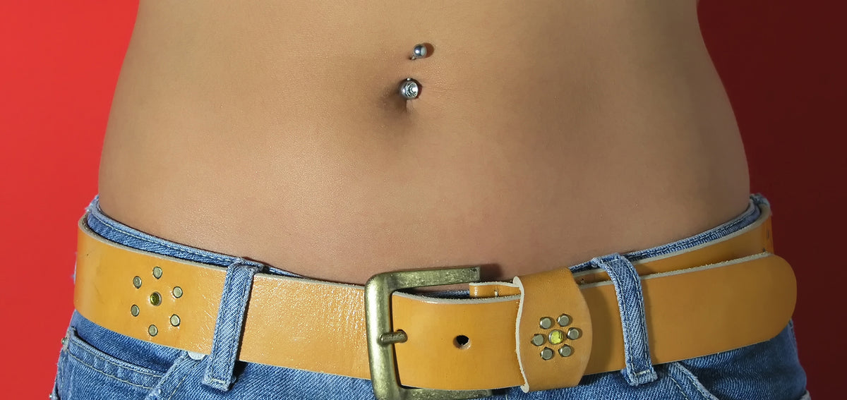 Midriff with a silver-tone belly button ring with crystal ends, above jeans and a tan studded leather belt