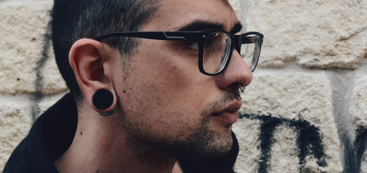 Man in black glasses wearing a black plug in his stretched lobe and a small septum ring