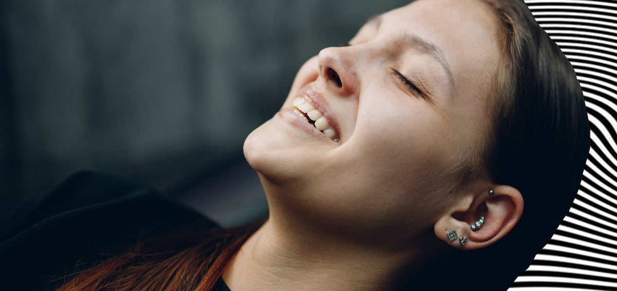 Laughing woman with her head tilted back, wearing a helix stud, a curved crystal cluster in her conch and lobe studs