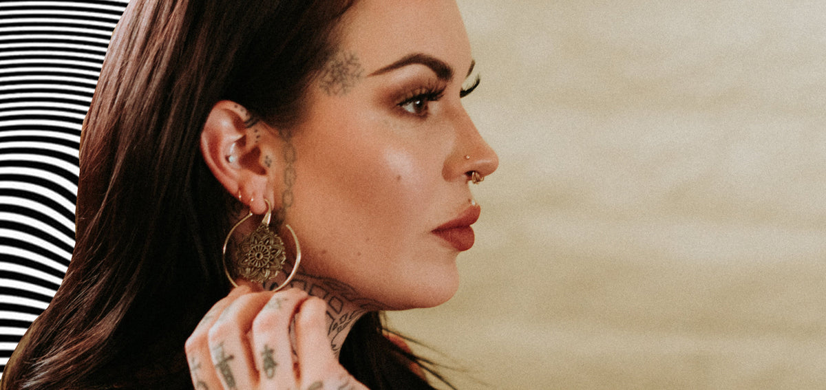 Tattooed woman in profile with a conch stud, lobe hoops, a gold-tone mandala hoop earring and a septum ring