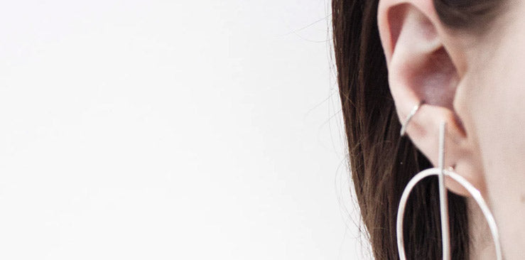 Ear with a thin silver-tone hoop in the conch and a large geometric silver-tone hoop earring in the lobe