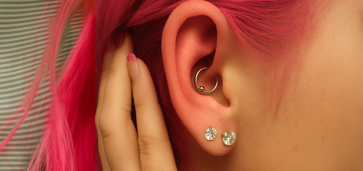 Ear framed by pink hair with a silver-tone captive bead ring in the daith and two crystal studs in the lobe