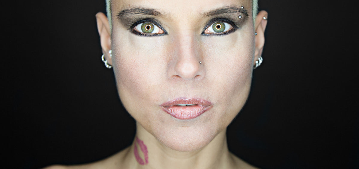 Woman facing the camera with a curved barbell in her outer eyebrow and silver-tone hoops in both lobes