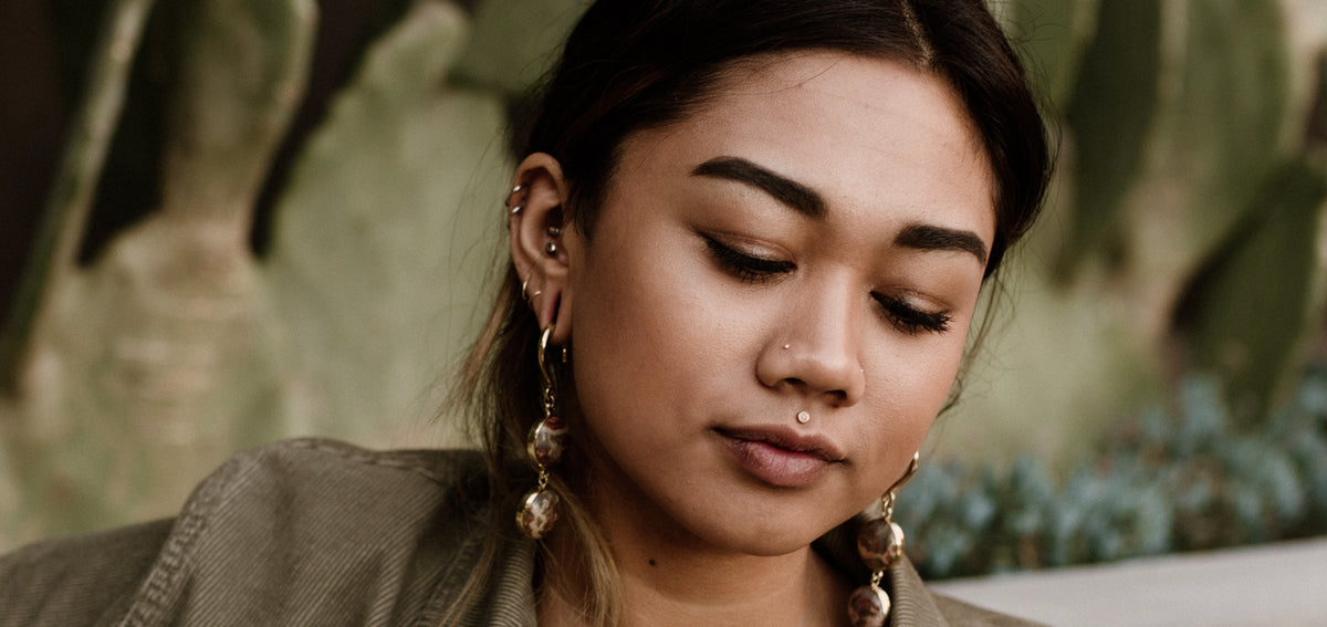 Woman looking down with a nostril stud, a medusa stud, several ear piercings and long beaded drop earrings