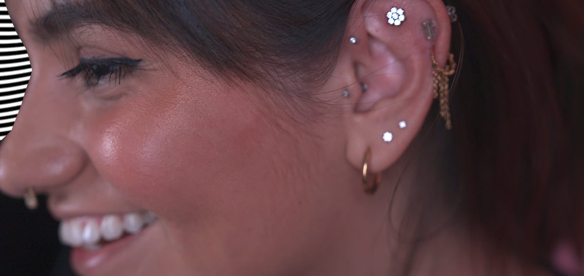 Smiling woman with a crystal flower stud in her flat, a draped gold-tone helix chain and crystal lobe studs