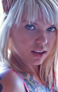 Blonde woman with a medusa stud above her upper lip, a small lip stud and tattoos on her chest