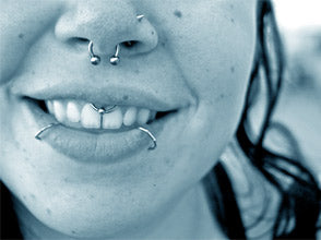 Smiling mouth with a septum horseshoe, a nostril hoop, a smiley ring above the front teeth and two lip rings