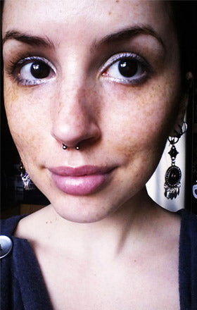 Woman with freckles wearing a silver-tone septum horseshoe with ball ends and ornate dangle earrings