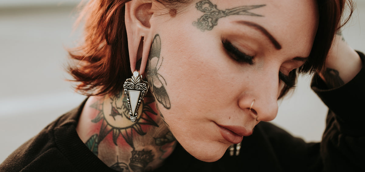 Tattooed woman with eyes closed, a thin nostril hoop and an ornate silver-tone ear weight in her stretched lobe