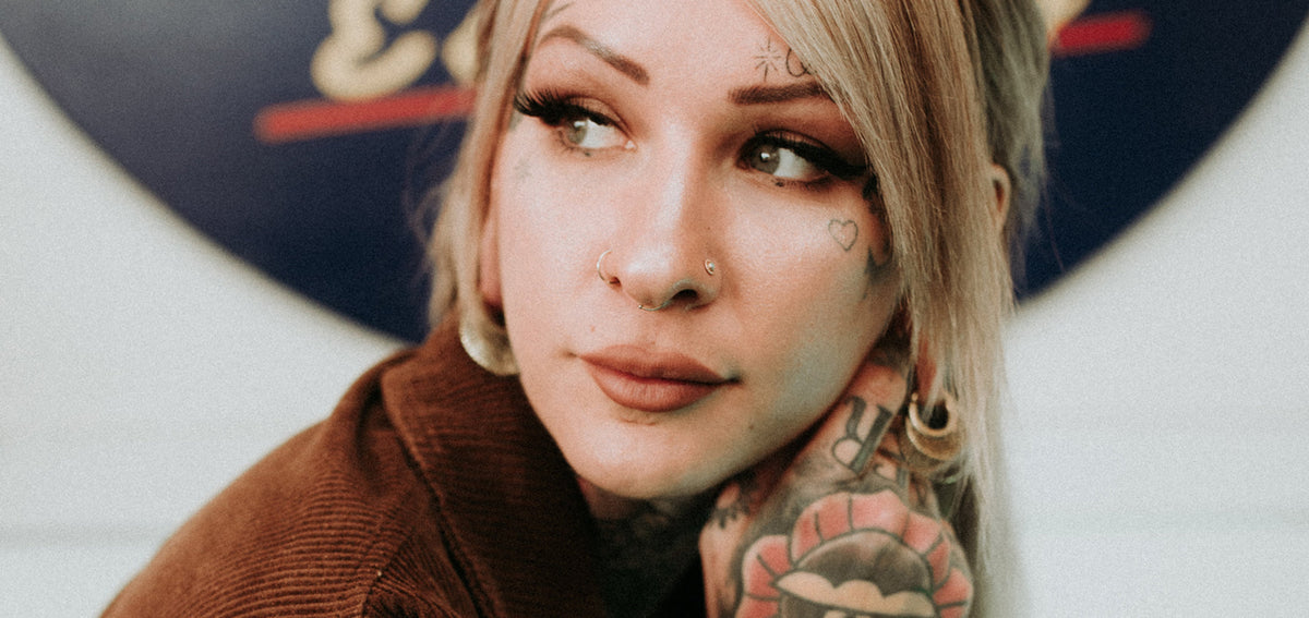 Tattooed blond woman wearing a gold-tone nostril hoop, a stud in the other nostril and a thin septum ring