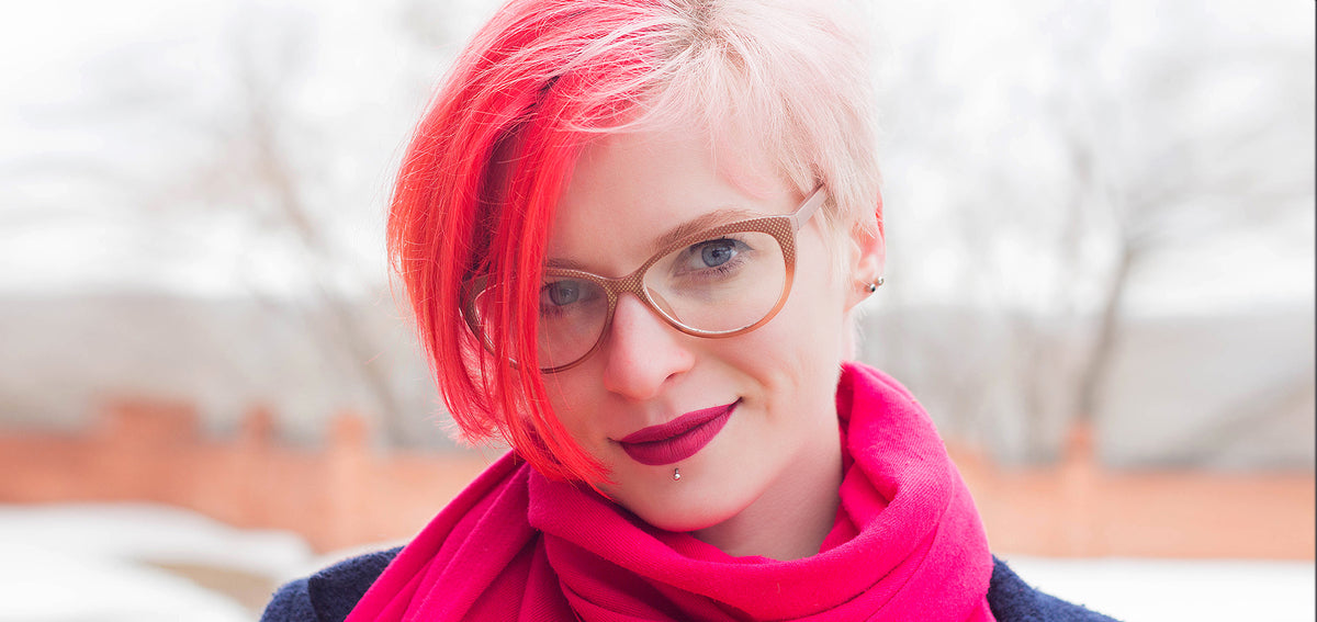 Woman with bright red hair and glasses wearing a labret stud below her lower lip and a pink scarf