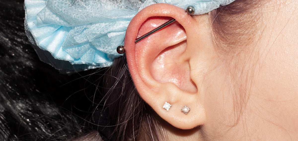 Ear with an industrial barbell across the upper cartilage and two clear crystal studs in the lobe