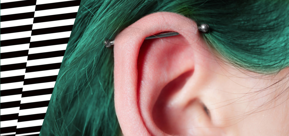 Close-up of an ear framed by green hair, with a silver-tone industrial barbell across the upper cartilage
