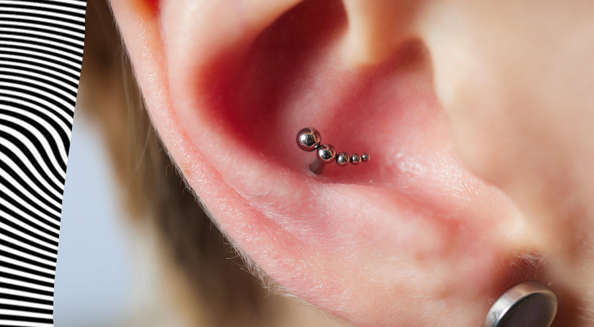 Close-up of an inner conch piercing with a curved stud of graduated silver-tone beads, and a plug in the lobe