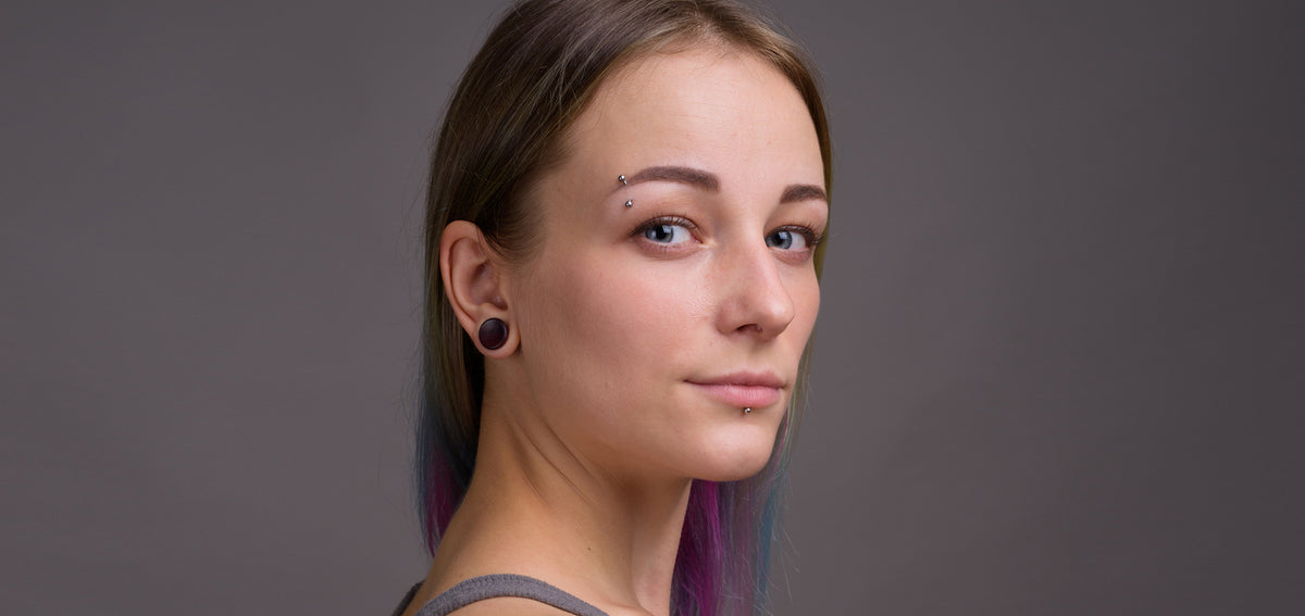 Woman with an eyebrow barbell, a labret stud below her lower lip and a dark plug in her stretched lobe