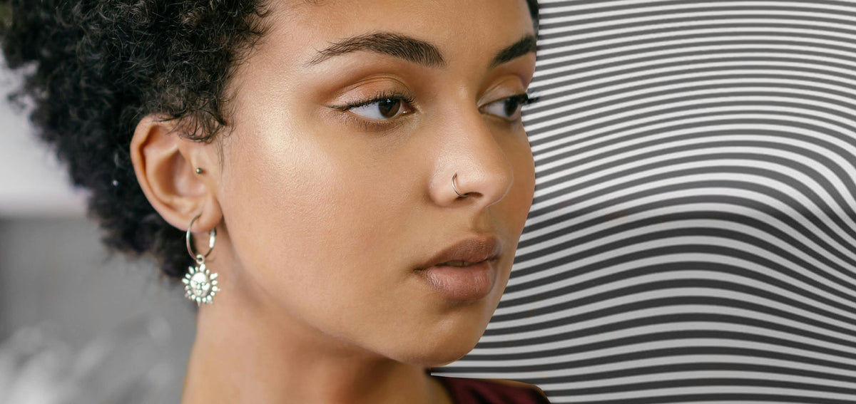 Woman with a thin silver-tone nostril hoop, a small ear stud and a silver-tone hoop earring with a sun charm