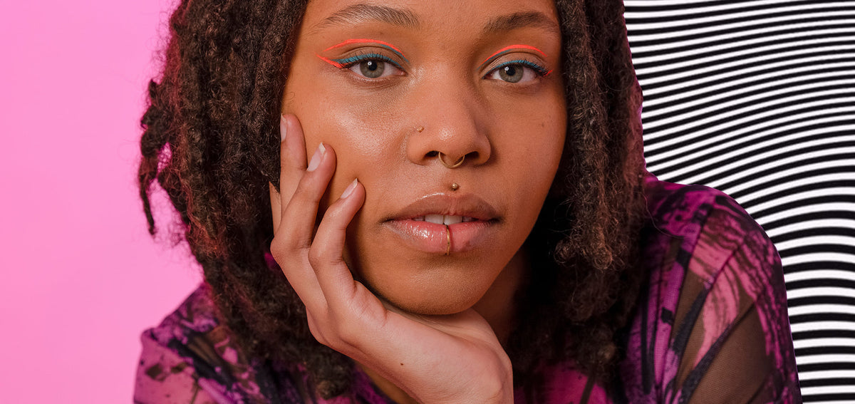 Woman resting her cheek on her hand, wearing a gold-tone nostril stud, septum ring, medusa stud and lower lip ring