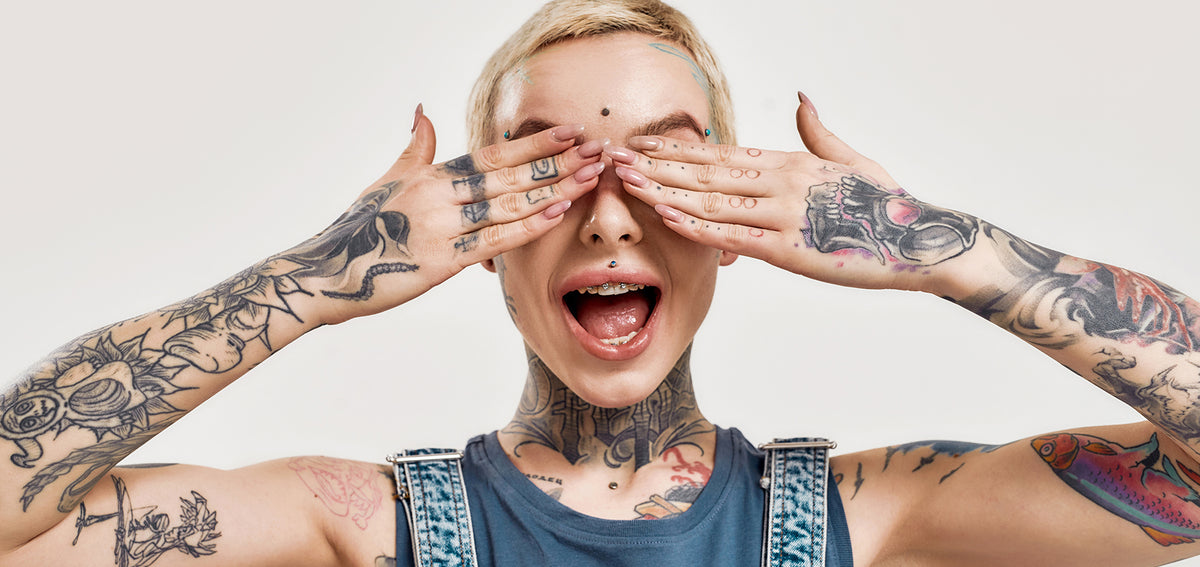 Tattooed person covering their eyes and shouting, with a stud between the brows and a philtrum stud above the lip