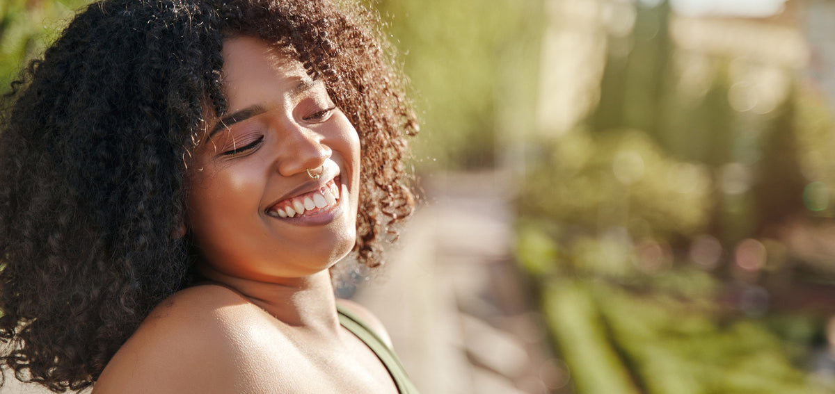 Smiling woman with curly hair and closed eyes wearing a gold-tone septum ring