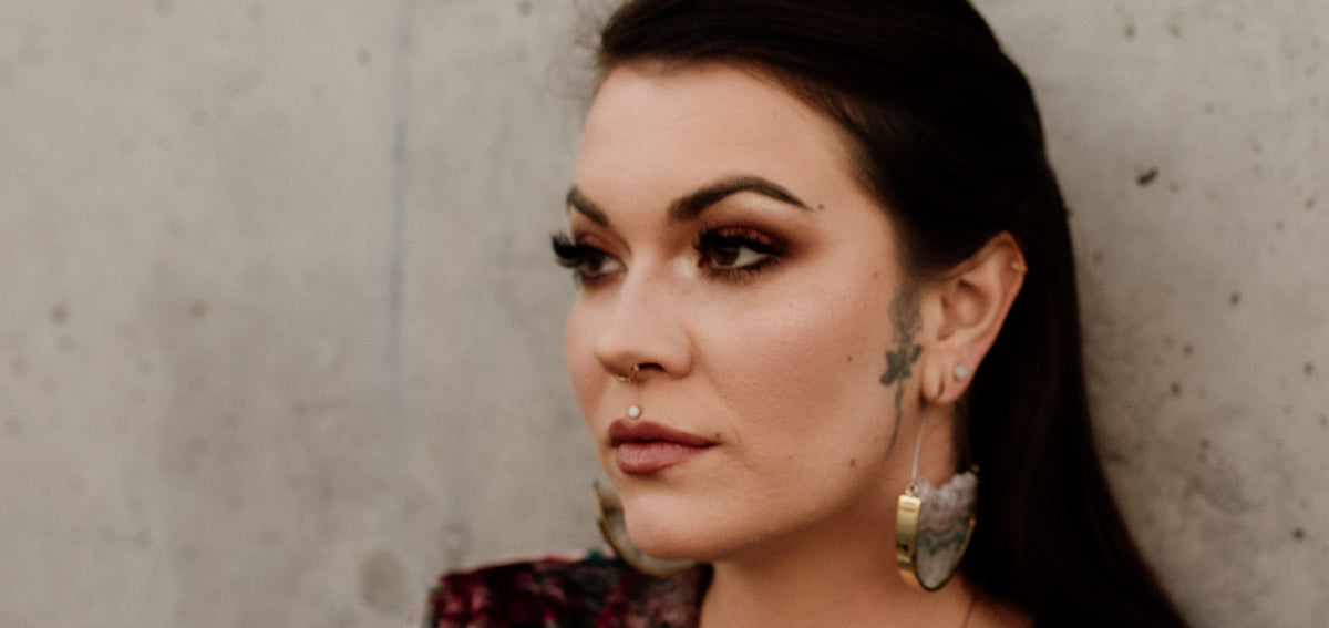 Woman with a white stone stud above her lip, a gold-tone nostril hoop and large gold-tone and stone half-moon earrings