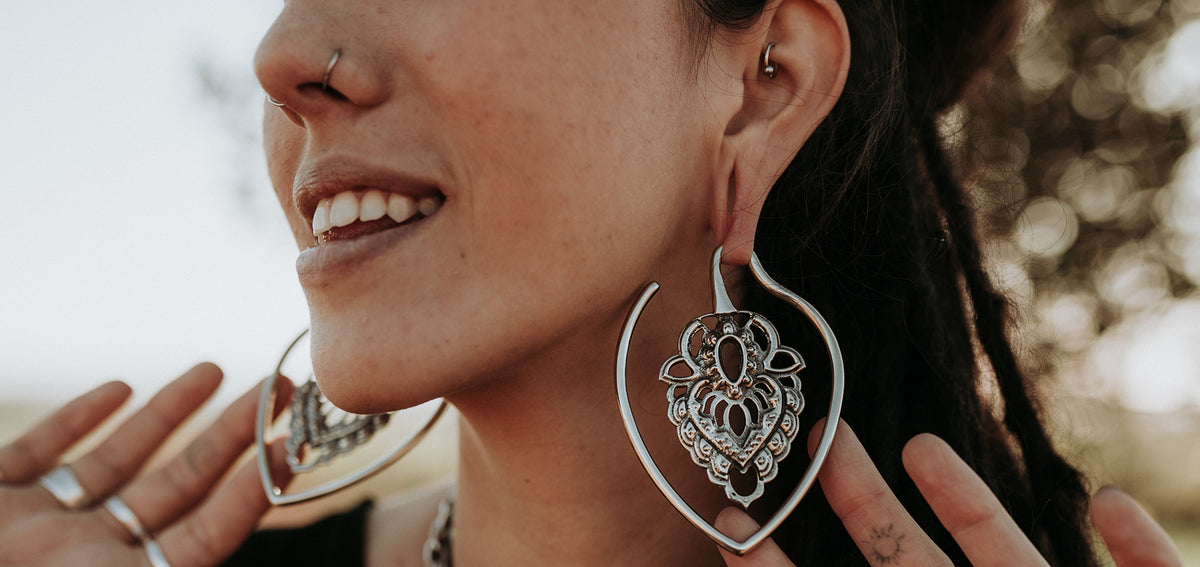 Smiling woman with a nostril ring, a small ring in her inner ear and large ornate silver-tone teardrop hoops