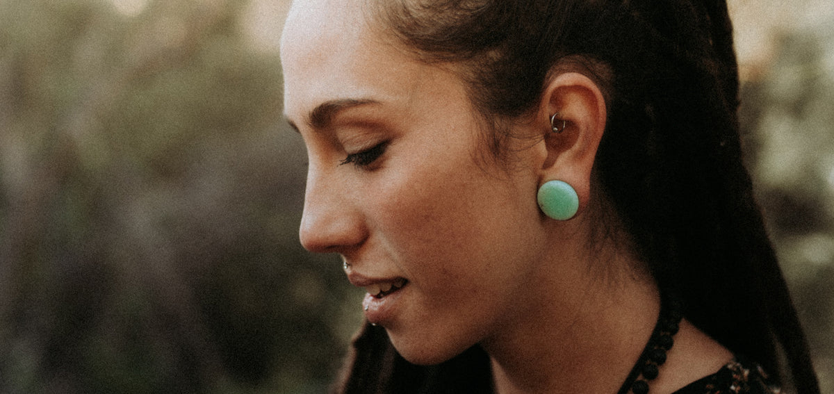 Woman in profile wearing a ring in her rook and a mint green plug in her stretched lobe