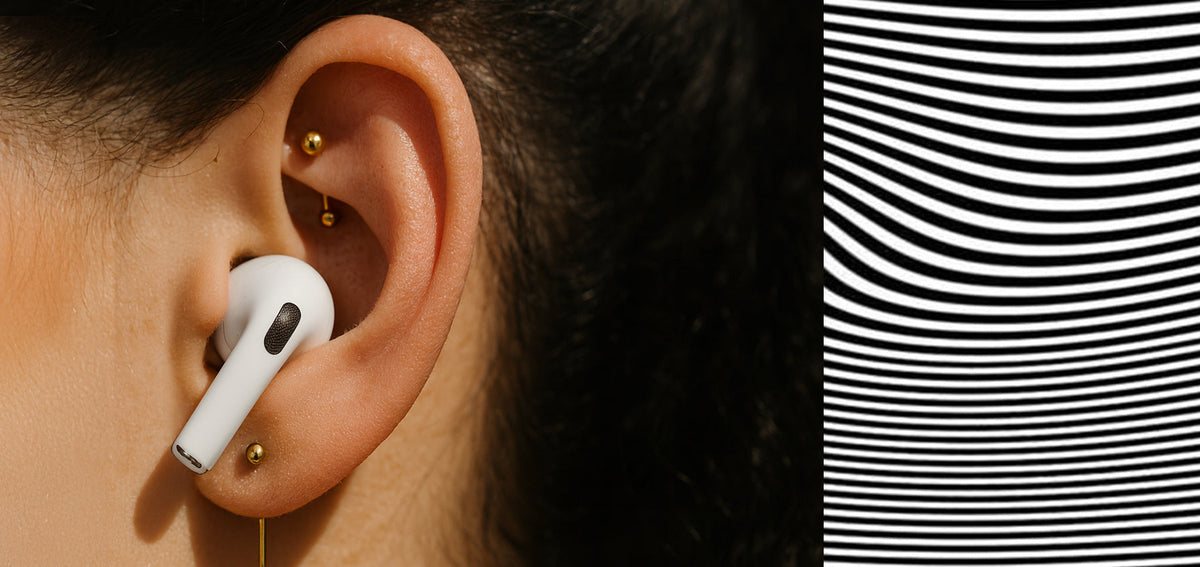 Ear wearing a white wireless earbud, with a gold-tone curved barbell in the rook and a gold-tone lobe stud
