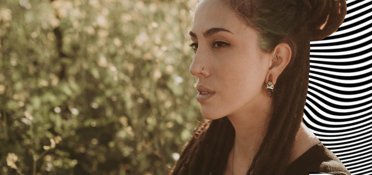 Woman with locs in profile, wearing a thin nostril hoop, a small ring in her rook and a sculpted metal lobe earring