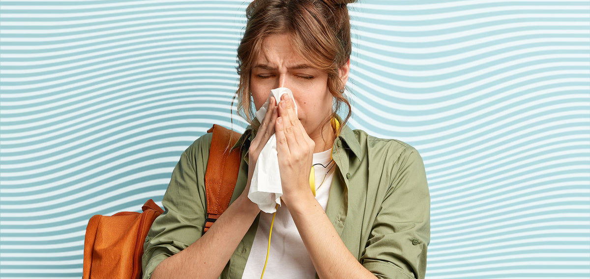 Woman with a backpack blowing her nose into a tissue, eyes squeezed shut