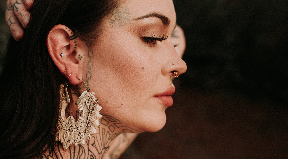 Woman in profile with stacked gold-tone septum rings, a nostril stud and a large carved cream ear weight