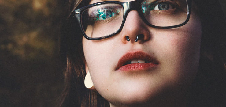 Woman in black glasses wearing a septum horseshoe ring, with a cream ear weight visible at her lobe