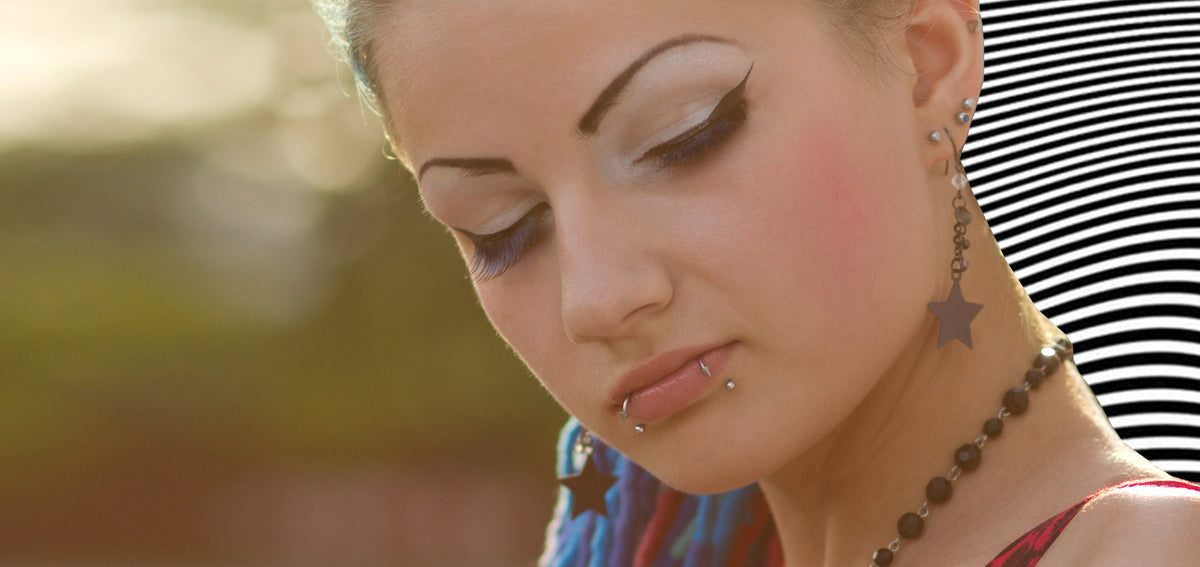 Woman with winged eyeliner and snake bite lip studs, wearing star dangle earrings and a beaded necklace