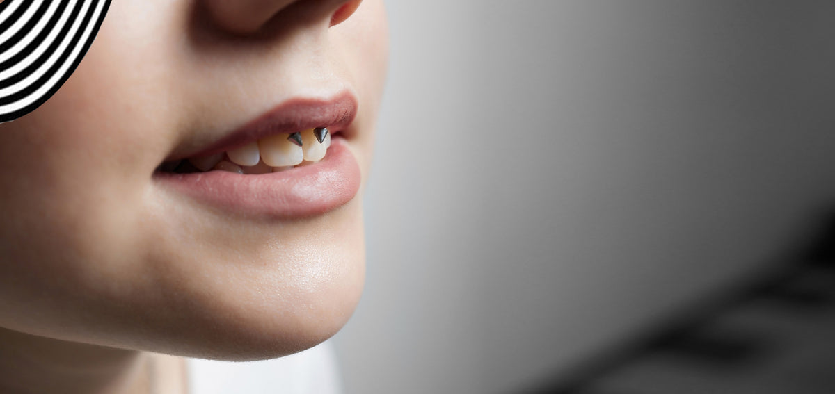 Close-up of parted lips with a smiley piercing, a ring with two small spikes resting over the upper front teeth