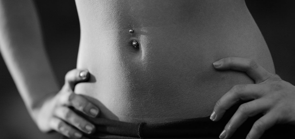 Midriff with hands on hips and a curved belly button barbell with ball ends, in black and white