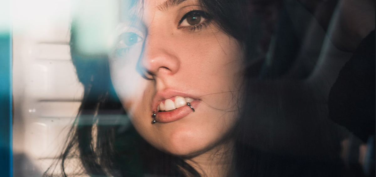 Woman seen through glass with silver-tone rings at both corners of her lower lip