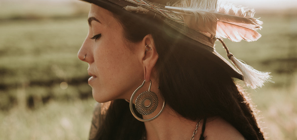 Woman in a feathered hat with a captive bead ring in her rook, a thin nostril hoop and a large mandala hoop earring